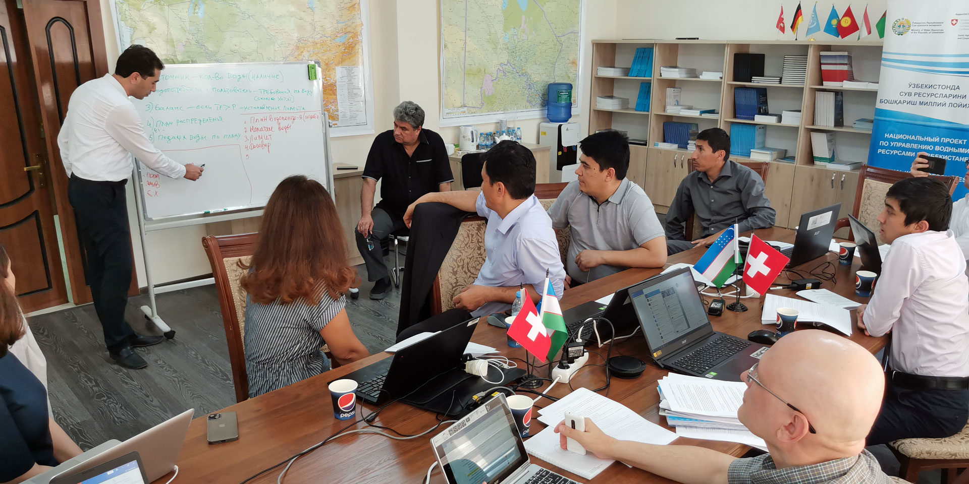 Frauen und Männer schauen auf eine weisse Wandtafel und folgen den Erklärungen eines Mannes.