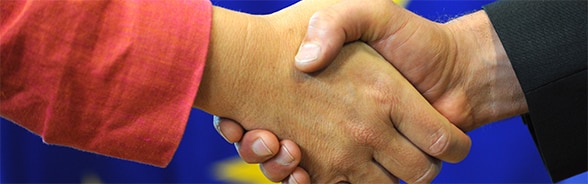 Foto eines Händedrucks vor einer Europaflagge