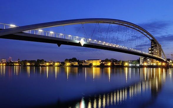 A floodlit bridge in the border region between Switzerland, Germany and France against the evening sky.