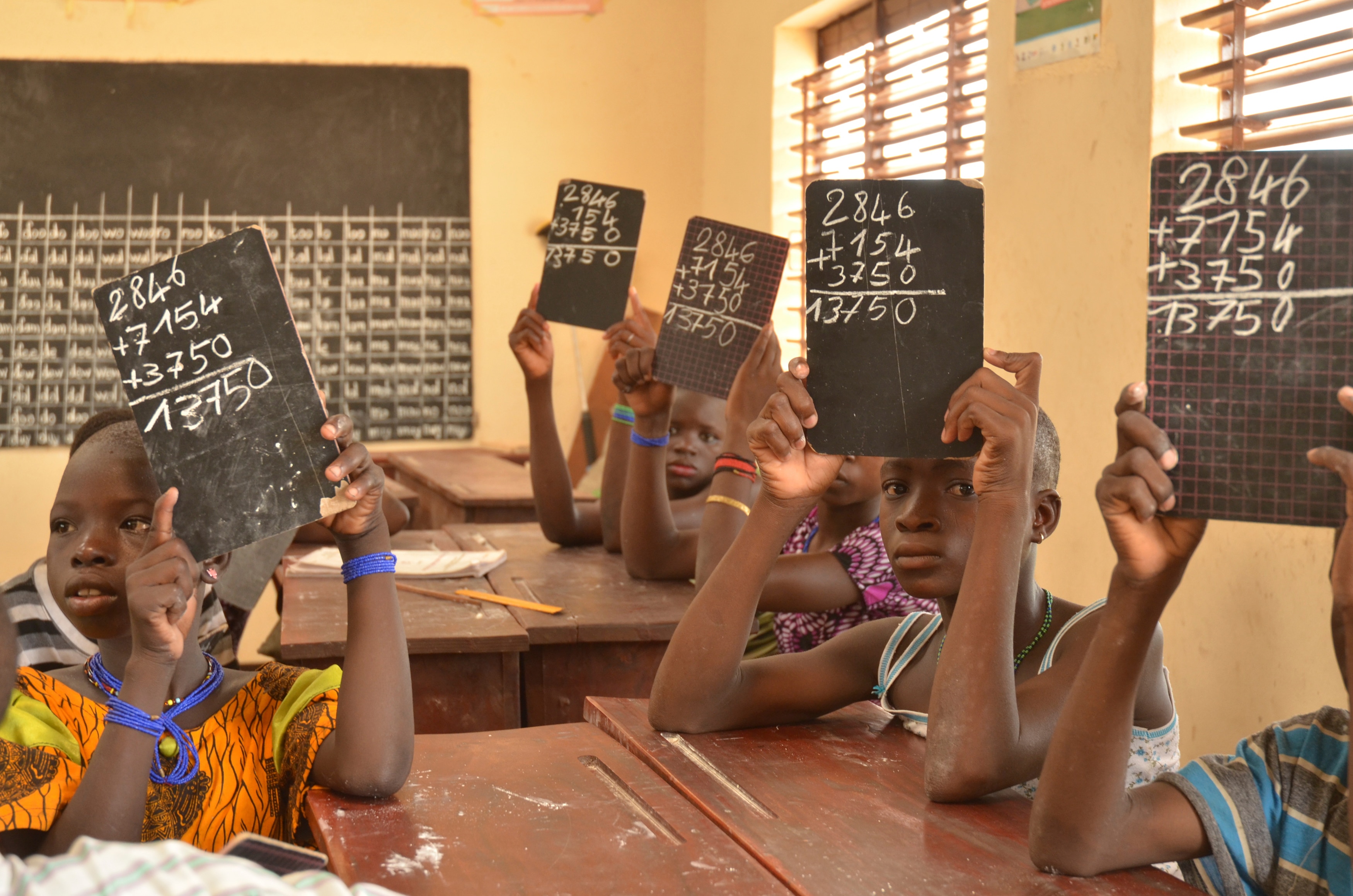 African schoolchildren sitting in a classroom holding up blackboards showing sums.