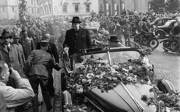 Winston Churchill steht bei seiner Ankunft in Zürich in einem blumenübersäten Fahrzeug.