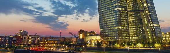 Modern high-rise in Frankfurt am Main, with glass facade, lit up against the evening sky.