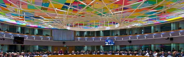Ein vollbesetzter Konferenzsaal mit bunter Decke im Europagebäude. Hier finden unter anderem die EU-Gipfel, multilaterale Gipfel und Ministertagungen statt.