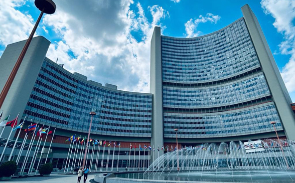  A multi-storey modern building with flags of different nations and a fountain in front.