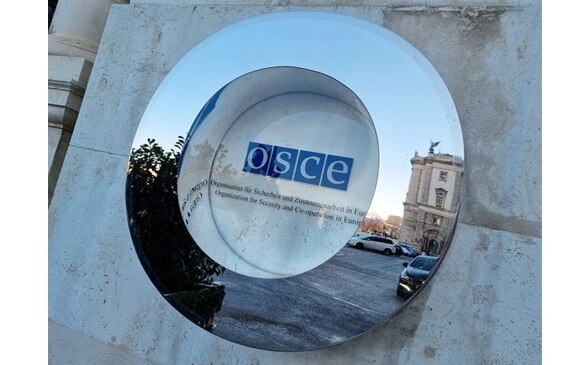 The OSCE's logo on a house wall behind glass.
