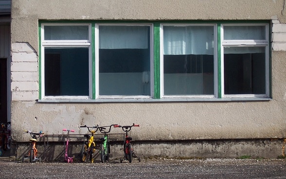 Quattro biciclette davanti a una scuola. La facciata, grigia e sgretolata, è solo invetriata. 