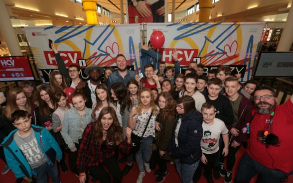 Alcuni youtuber e una quarantina di ragazzi e ragazze in piedi davanti a un cartellone colorato durante un evento molto animato.