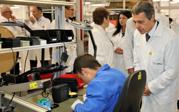 Federal Councillor Ignazio Cassis observing a young apprentice of a vocational training project during her work.