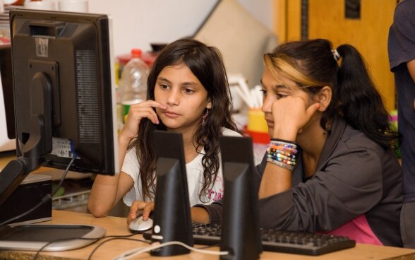 Two Roma girls sitting in front of a computer.