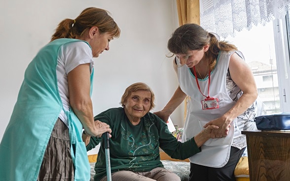 Two female healthcare workers helping an elderly woman to stand up.