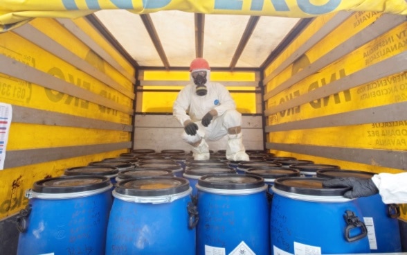 Mann in Schutzanzug auf mit Pestiziden gefüllten Fässern im Lastwagen.