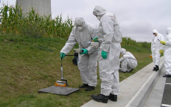 Alcuni collaboratori misurano il tasso di radioattività indossando una tuta di protezione bianca.