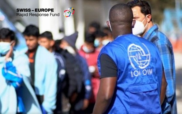 Un mediatore culturale dell’OIM discute con un migrante per fornirgli un sostegno. Sullo sfondo si scorgono altri migranti.