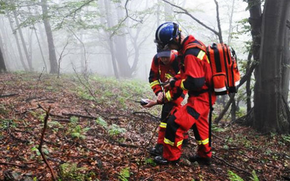 Two disaster protection officers check their equipment in a wood.