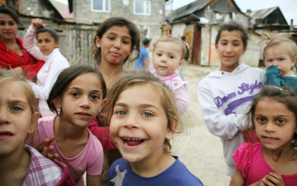 Nove bambini e una donna guardano in camera.