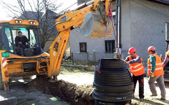 A man sitting in a digger and three other workmen working on the sewerage system.